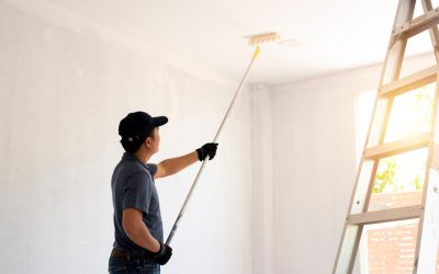 Asian rear view of a male painter drawing a wall with paint roll Asian rear view of a male painter drawing a wall with paint roller and a separate tank from a large empty space with wooden stairs.